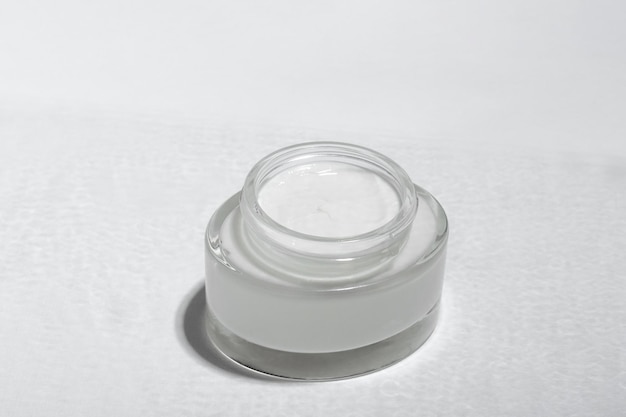 Creme cosmético ou máscara em uma jarra de vidro com sombras duras das folhas em um fundo branco Cuidado orgânico natural para a pele do rosto e do corpo Vista de cima