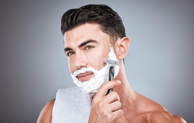 Creme de barbear facial e homem com navalha em estúdio isolado em um fundo cinza Limpeza de cuidados com a pele e modelo masculino pensativo com espuma de produto facial ou gel para barbear para bem-estar, saúde e higiene