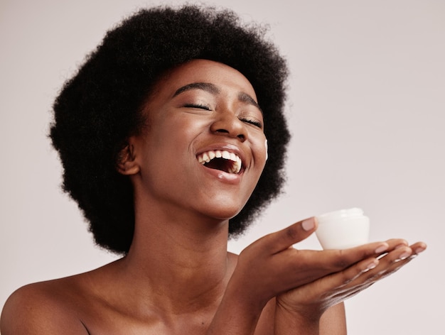 Creme de beleza para cuidados com a pele e uma mulher negra em estúdio feliz com recipiente cosmético dermatológico modelo estético com mãos para colocação de produtos para saúde, bem-estar e pele facial brilha fundo cinza