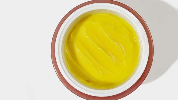 Creme de rosto amarelo em uma jarra em cosméticos hidratantes de fundo branco