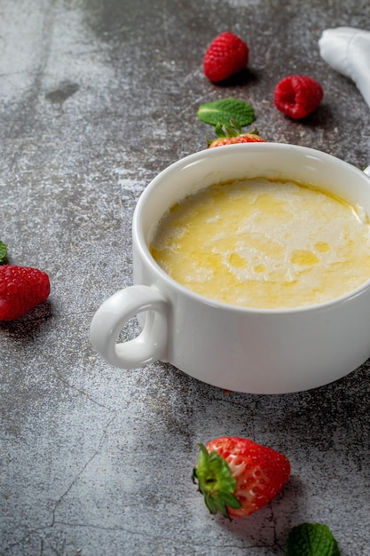 Creme de trigo, pudim de sêmola com manteiga e framboesas frescas e morangos com hortelã em um copo branco contra uma mesa de pedra cinza. Um café da manhã saudável em um restaurante