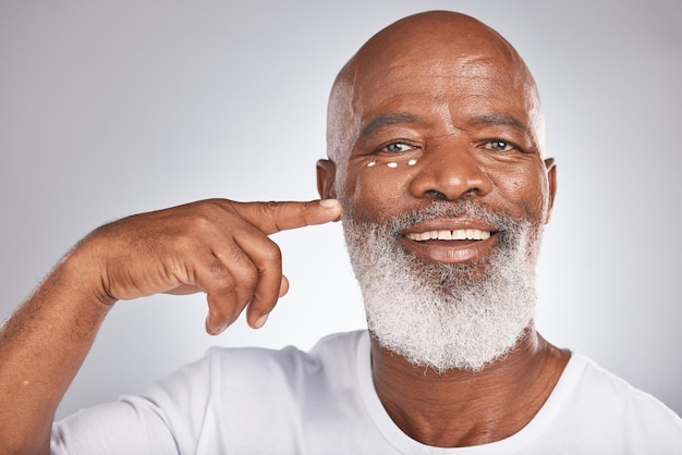 Creme facial de beleza e cuidados com a pele do homem negro em estúdio para autocuidado com dermatologia e cosméticos para a pele Retrato de homem sênior feliz com loção na pele para brilho, saúde e bem-estar em cinza