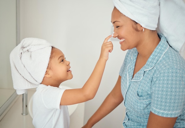 Foto creme facial de mãe e menina no banheiro aplicam cosméticos de beleza e produto de loção para rotina matinal de chuveiro sorriso de felicidade ou mãe feliz e criança adoram creme de cuidados com a pele em casa