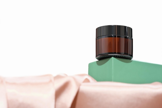 creme facial em frasco de vidro âmbar no pódio verde ou pedestal em tecido de cetim de seda simulado para apresentação de produto ecológico natural
