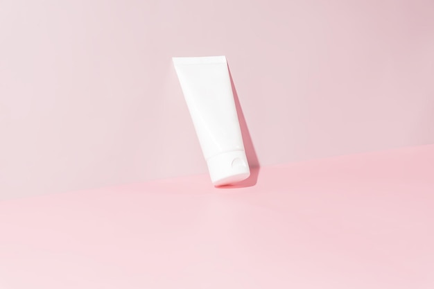 Creme facial ou para as mãos em tubo de plástico branco sobre fundo rosa Conceito de cuidados com a pele Mock up estilo minimalismo