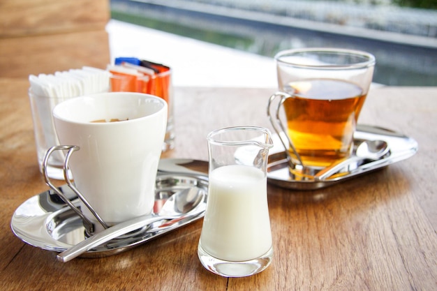 Creme für Kaffee oder Tee mit einer Tasse Kaffee und einer Tasse Tee mit Seidenpapier und Zucker auf dem Holztisch