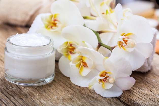 Creme hidratante e orquídea em fundo de madeira