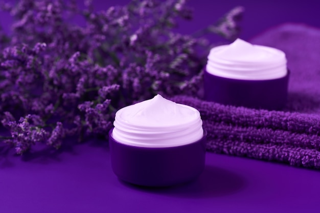 Creme ou loção facial de noite natural, cosmético orgânico para hidratar a pele com toalha e flores ao fundo.