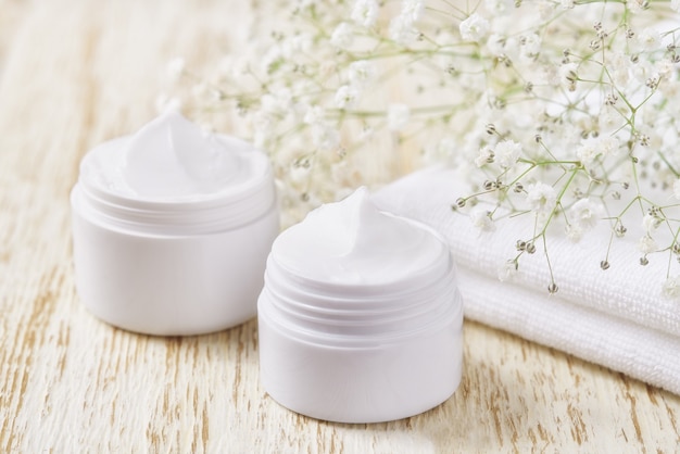 Creme ou loção natural para o rosto, produto cosmético orgânico para hidratar a pele com toalha e flores no fundo.