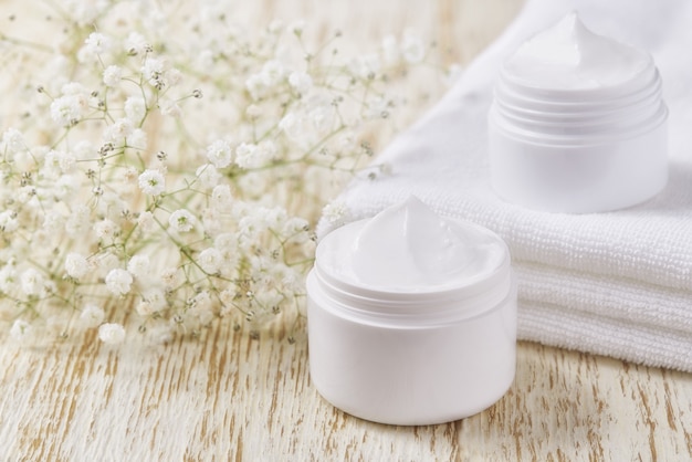 Creme ou loção natural para o rosto, produto cosmético orgânico para hidratar a pele com toalha e flores no fundo.