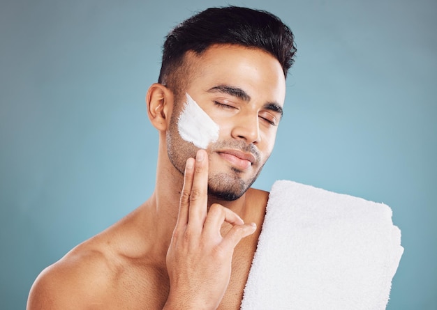 Creme para a pele do rosto e rotina matinal facial do homem para cuidados de beleza Jovem indiano hidratar o tratamento da pele e cuidar do bem-estar ou cuidar do corpo com dermatologia saudável no estúdio de fundo azul