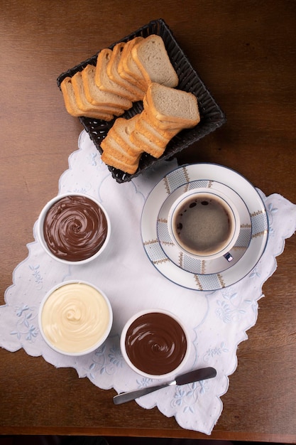Cremes de chocolate de avelã e chocolate branco com waffles na mesa de café da manhã e cesta de pão vista superior