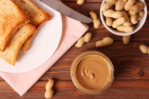 Cremige Erdnussbutter und Erdnussbohnen auf Draufsicht des hölzernen Hintergrundes