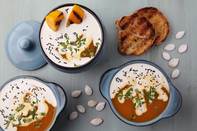 Cremige Kürbissuppe mit cremefarbenen Schwarzkümmel-Kräuter-Kürbiskernen und geröstetem Brot auf einem blauen Holztisch