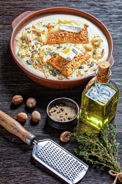 Cremige vegane Blumenkohlsuppe mit Toast mit geschmolzenem Camembertkäse in einer Tonschüssel auf einem rustikalen Holztisch, vertikale Ansicht, französische Küche