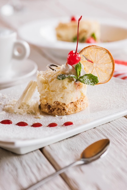 Cremiges Orangen-Dessert, das auf einem quadratischen Teller serviert wird. Köstlicher Kuchen mit Dekoration aus weißer Kirschschokolade und Minze, Nahaufnahme