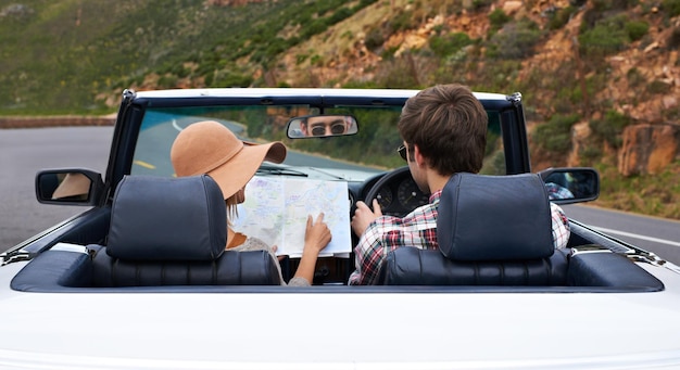 Creo que deberías haber girado aquí Vista trasera de una pareja joven leyendo un mapa mientras están sentados en un automóvil