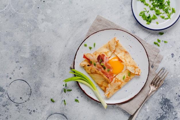 Crepe com ovo frito, queijo, bacon e cebolinha no café da manhã em uma superfície de concreto cinza claro