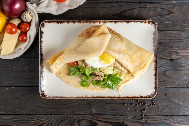 Crepe com salada e ovo. Prato principal quente no café da manhã ou almoço de panquecas com ovo frito, filé de frango, legumes e salada