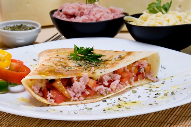 Crepe de presunto e tomate, com ingredientes no fundo.