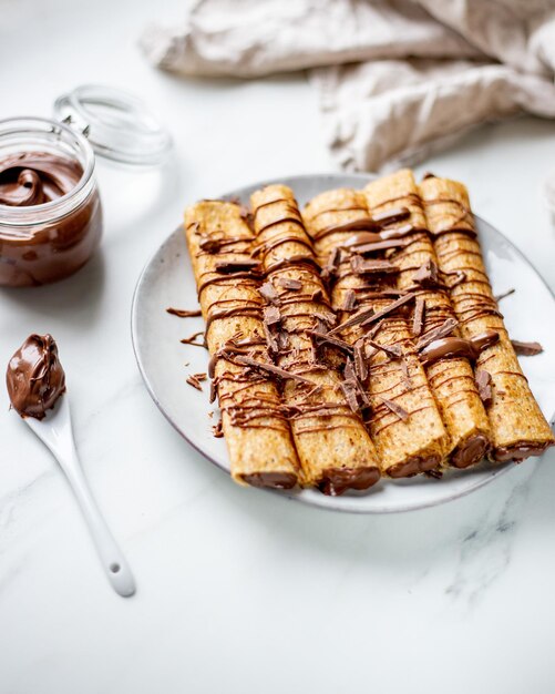 Foto crepe francés relleno de dulce de caramelo y decorado con bayas de dulce de chocolate, azúcar de ricino y hojas de menta sobre fondo de mármol con espacio para copiar