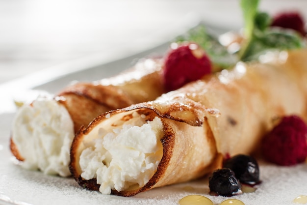 Crepe con requesón de cerca. Postre laminado casero con frambuesas en plato blanco.