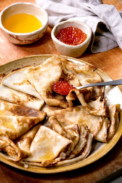 Crepe suzette de pansakes finos servidos con caviar rojo y mantequilla derretida en un plato de cerámica sobre una pared de piedra marrón.