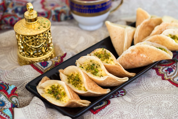 Crepes árabes tradicionales de kataif rellenos de crema y pistachos, preparados para iftar en Ramadán, oud en oro, en paisley
