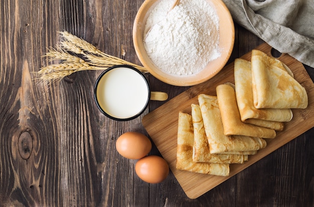 Crepes caseiros frescos com ingredientes e espigas de trigo em fundo de madeira rústico. vista do topo.