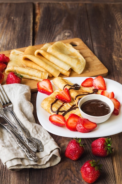 Crepes caseiros frescos com morangos e calda de chocolate em fundo de madeira rústico.