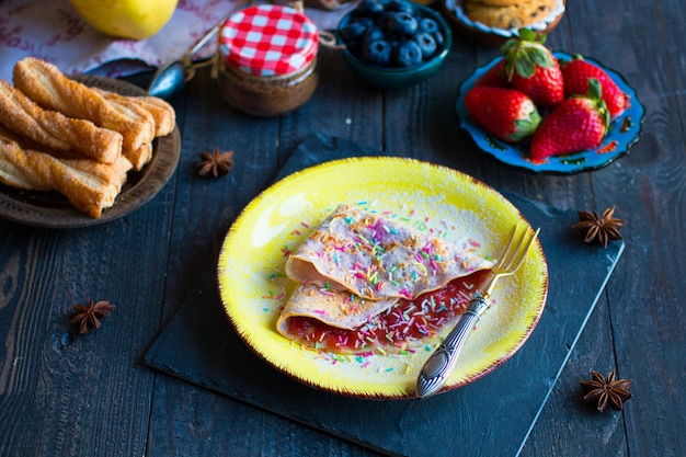 Crepes caseiros frescos, servidos em um prato com morangos e mirtilos em um fundo escuro de madeira