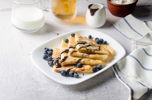 Crepes caseiros, saborosas panquecas finas com chocolate e frutas em um prato branco no café da manhã com uma xícara de chá. cozinha tradicional russa.