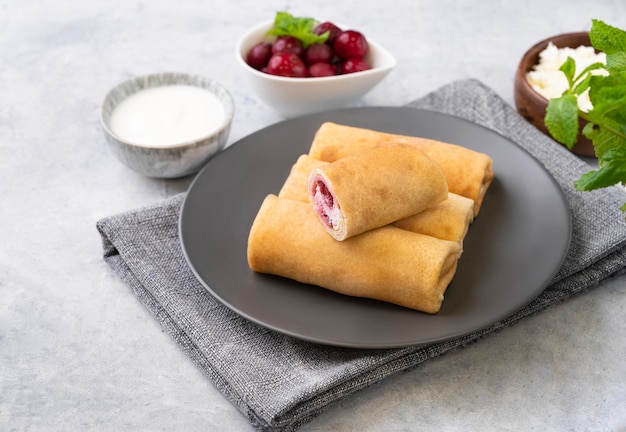 Crepes caseros con cereza y requesón en un plato sobre un fondo azul con crema agria