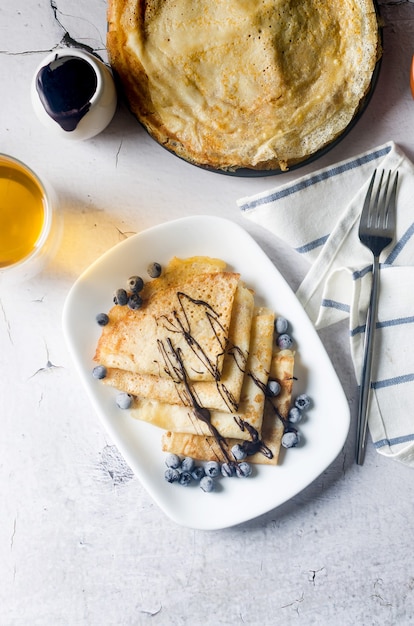 Crepes caseros, deliciosos panqueques finos con chocolate y bayas en un plato blanco para desayunar con una taza de té. Cocina tradicional rusa.