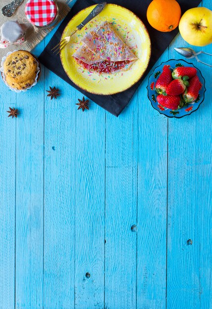 Crepes caseros frescos servidos en un plato con fresas y arándanos sobre un fondo de madera azul claro