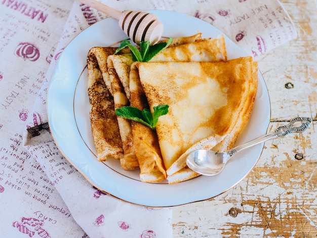 Crêpes, dünne Pfannkuchen mit Honig und Minze auf einem weißen Teller.