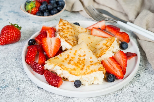 Crepes finos com queijo ricota e morangos frescos em um fundo cinza e concreto.