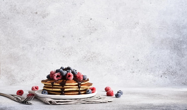 Crepes con frambuesas y arándanos y salsa de chocolate para desayunar sobre un fondo claro de hormigón