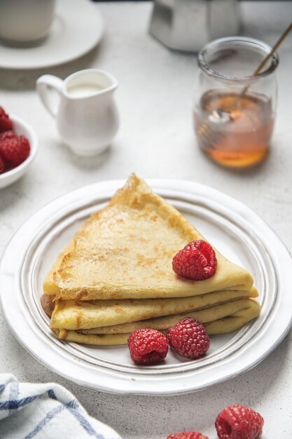 Crepes con frambuesas y miel en mesa blanca