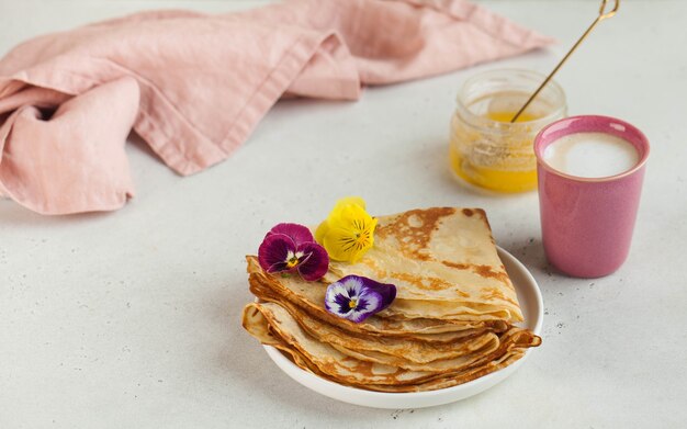 Crepes franceses, panquecas decoradas com flores, uma caneca de cappuccino e mel. Conceito de café da manhã, sobremesa.