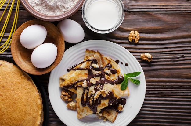 Crepes franceses planos con salsa de chocolate, nueces, huevos y harina en la mesa de la cocina de madera