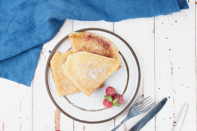 Crêpes gefüllt auf Platte dünne Pfannkuchen Blini weißer Holztisch