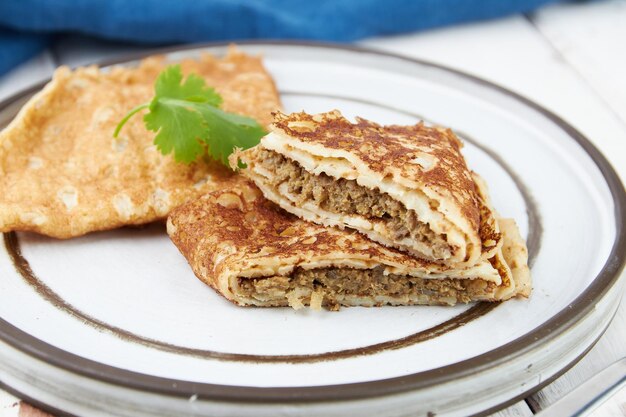 Crêpes gefüllt auf Platte dünne Pfannkuchen Blini weißer Holztisch