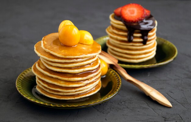 Crepes con la miel, el chocolate y las bayas en un fondo gris.