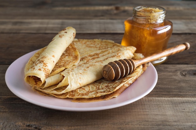 Crepes con miel sobre fondo de madera en plato rosa con cuchara de miel. Copie el espacio.