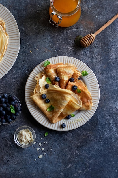 Crêpes mit Honig, Minzblättern, Heidelbeeren auf grauem Steinhintergrund. schließen sie mit copyspace. Leckere Crêpes, dünne Pfannkuchen