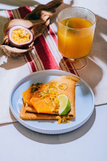 Foto crepes oder dünne pfannkuchen mit köstlichen passionsfrüchten und limetten. ein glas mit mango-nektar.