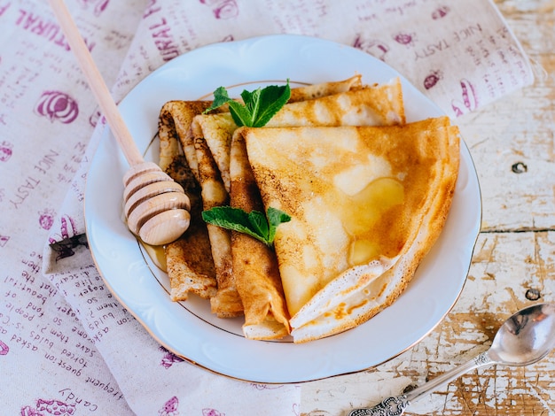 Crepes, panquecas finas com mel e hortelã em um prato branco.