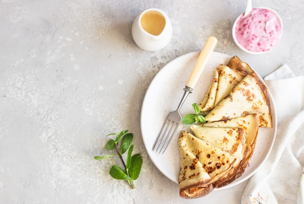 Crepes, panqueques finos con yogurt rosado, mermelada y miel decorados con menta en un plato de cerámica