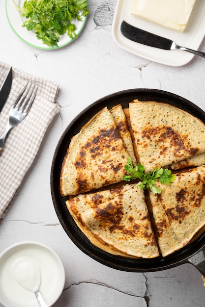 Crepes de queso de primer plano con verduras dobladas en un triángulo en una sartén de hierro fundido servido con cubiertos y mantequilla sobre un fondo de hormigón Concepto de semana de panqueques plano